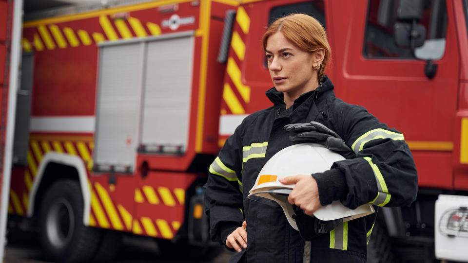 a female fire fighter holding her helmet in front of a fire truck