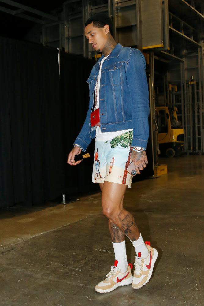 Jordan Clarkson in shorts, trainers and a denim jacket with a tiny red bag around his neck, walking through an airport