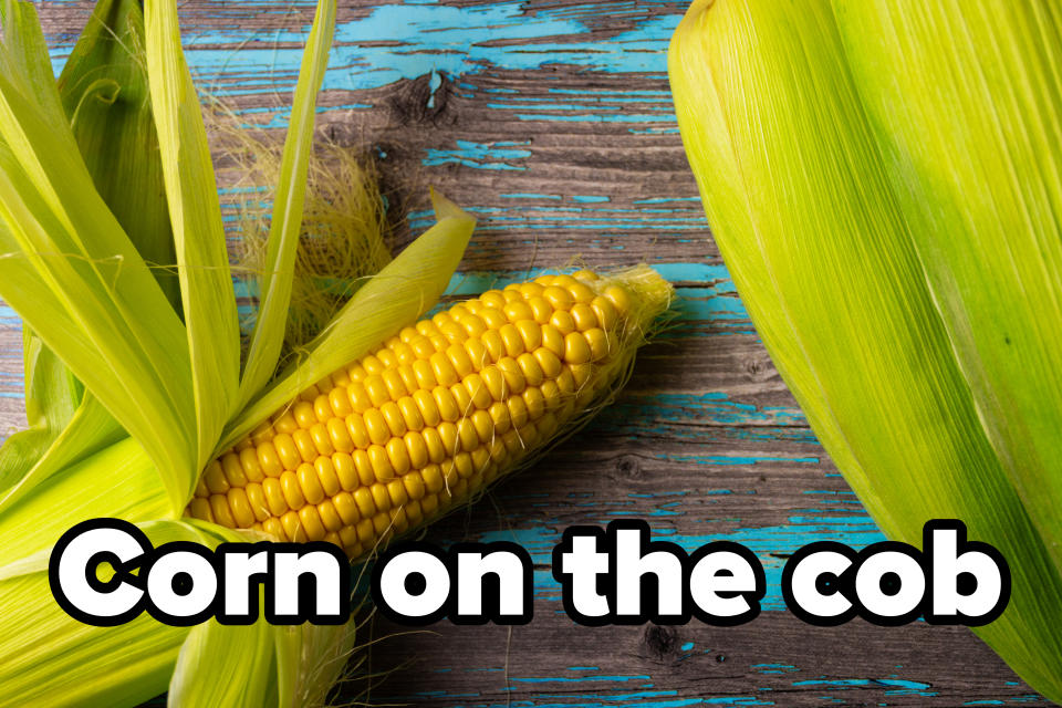 A peeled ear of corn on a wooden table with peeling husks, next to an unpeeled ear of corn