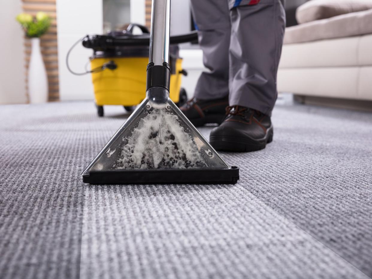 Low Section Of A Person Cleaning The Carpet With Vacuum Cleaner In Living Room