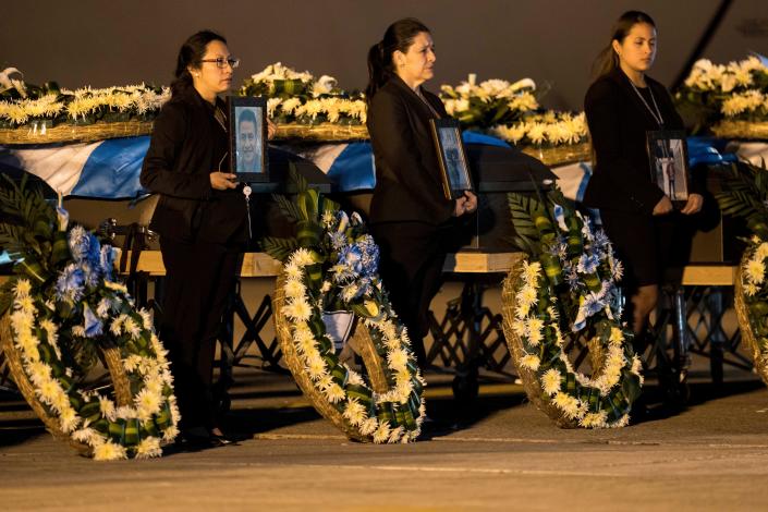 Foreign Ministry officers hold portraits beside the coffins of Guatemalan migrants whose remains arrived at the La Aurora Air Force Base in Guatemala City on Tuesday, April 11, 2023. The Mexican air force transported the bodies of 17 migrants who died in a fire at an immigration detention center in Juárez, Mexico.