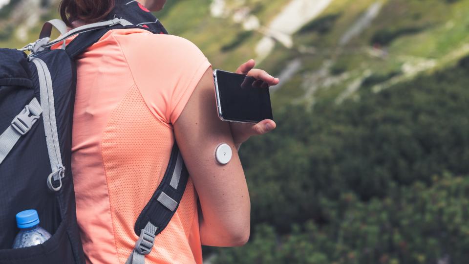 Active life of diabetics, woman hiking and checking glucose level with a remote sensor and mobile phone