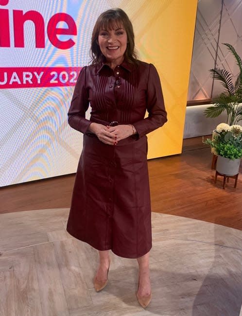 lorraine kelly stands smiling in a fit and flare style burgundy dress