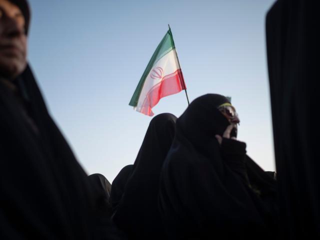 Women stand under an Iranian flag during a rally in support of the hijab.