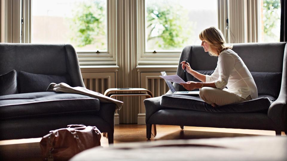 Shot of a mature woman working on a laptop in her living room after a trip.