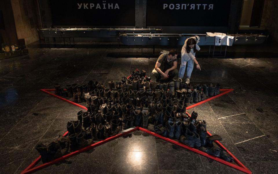 People look at boots that belonged to Russian soldiers as the 'Ukraine Crucifixion' exhibition opens in Kyiv - ROMAN PILIPEY/EPA-EFE/Shutterstock