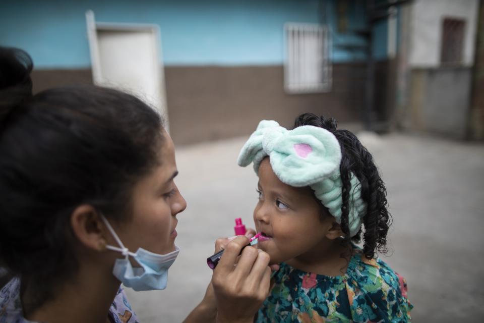 Elena Escalante helps her 3-year-old daughter Zaii prepare for a homespun beauty pageant in the Antimano neighborhood of Caracas, Venezuela, Friday, Feb. 5, 2021. Neighbors in the hillside barrio gathered for the carnival pageant tradition to select their child queen for the upcoming festivities. (AP Photo/Ariana Cubillos)