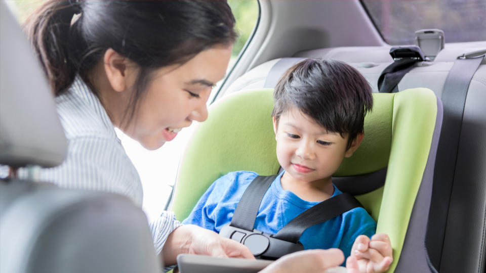 Pictured is a woman strapping her son into a car seat. 