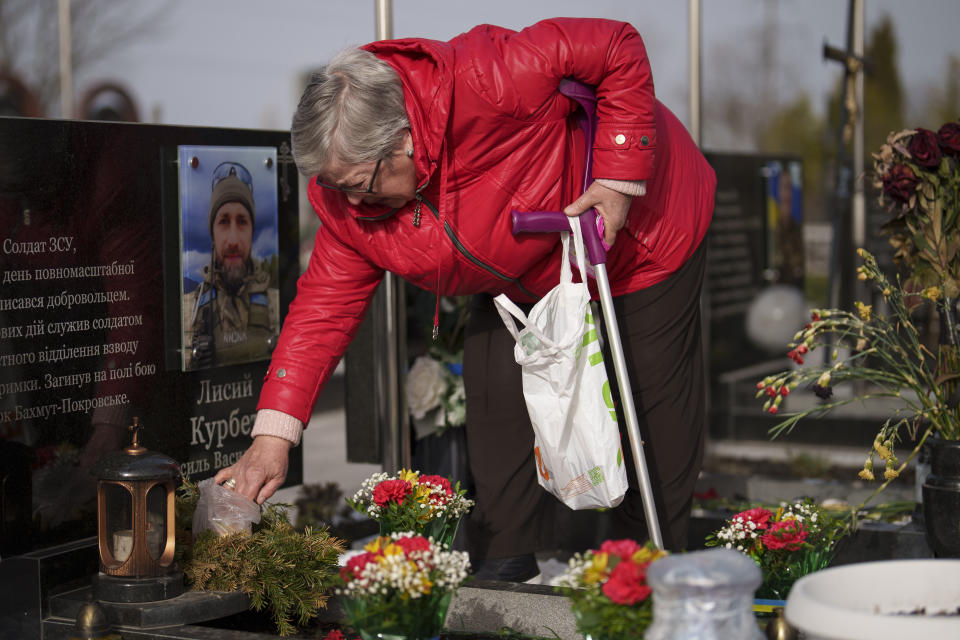 A relative places a bag of candies on the grave of a Ukrainian serviceman during a commemoration for the victims of the Russian occupation at a cemetery in Bucha, Ukraine, Sunday, March 31, 2024. Ukrainians mark the second anniversary of the liberation of Bucha, during which Russian occupation left hundreds of civilians dead in the streets and in mass graves in Bucha during the initial months of the Russian invasion in 2022. (AP Photo/Vadim Ghirda)