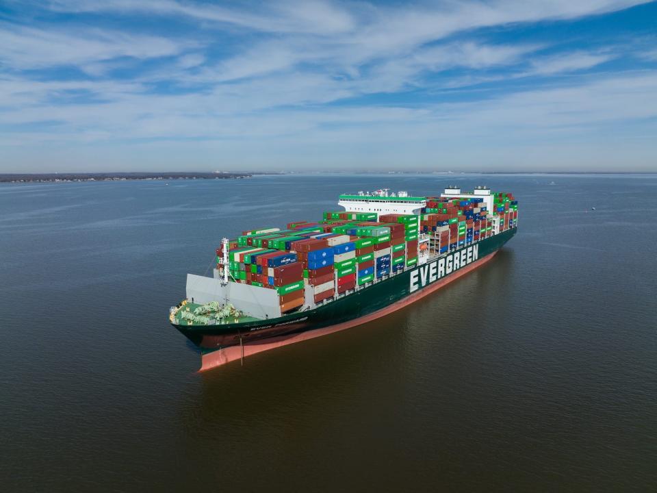 container ship labeled Evergreen across the side stacked high with green red and blue boxes in the open ocean with a coast in the distance