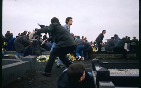 Following a grenade attack, people, including a television crew, take shelter on the ground in a cemetery during the funeral for three IRA members. - Credit: Bernard Bisson/Sygma