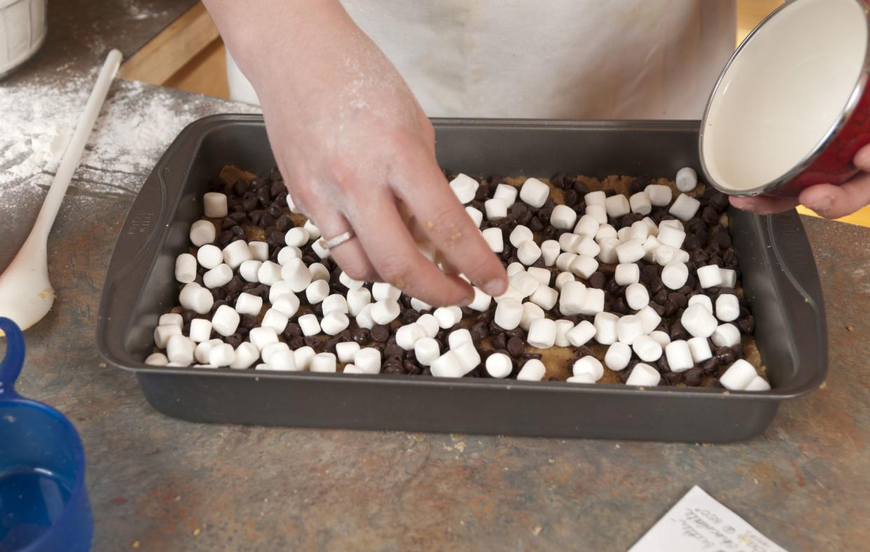 Hands sprinkling marshmallows onto a baked dessert.