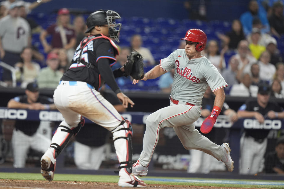 Philadelphia Phillies' J.T. Realmuto, right, heads home to score on a double by Bryce Harper, as Miami Marlins catcher Christian Bethancourt waits for the throw during the eighth inning of a baseball game, Friday, May 10, 2024, in Miami. (AP Photo/Wilfredo Lee)