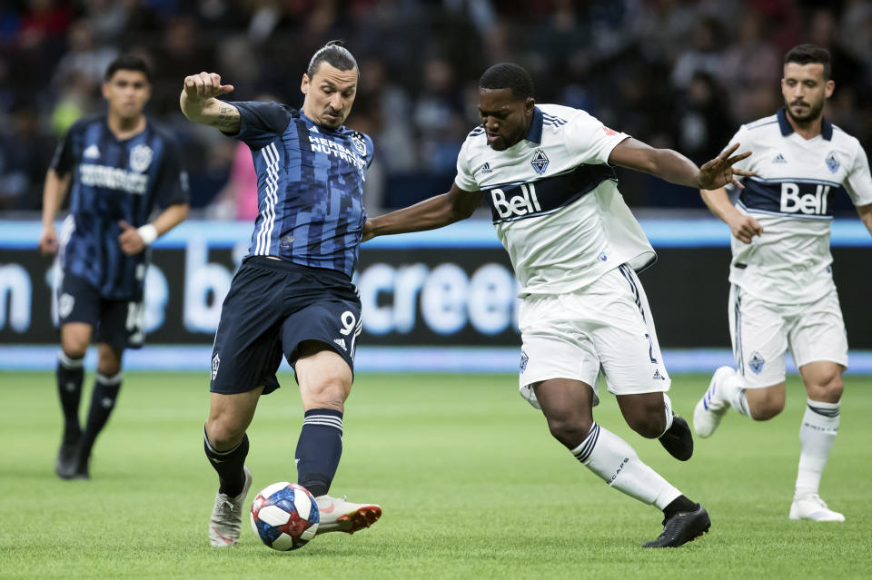 Los Angeles Galaxy's Zlatan Ibrahimovic (9) passes the ball as Vancouver Whitecaps' Doneil Henry (2) defends during the first half of an MLS soccer game in Vancouver, British Columbia, Friday, April 5, 2019. (Darryl Dyck/The Canadian Press via AP)