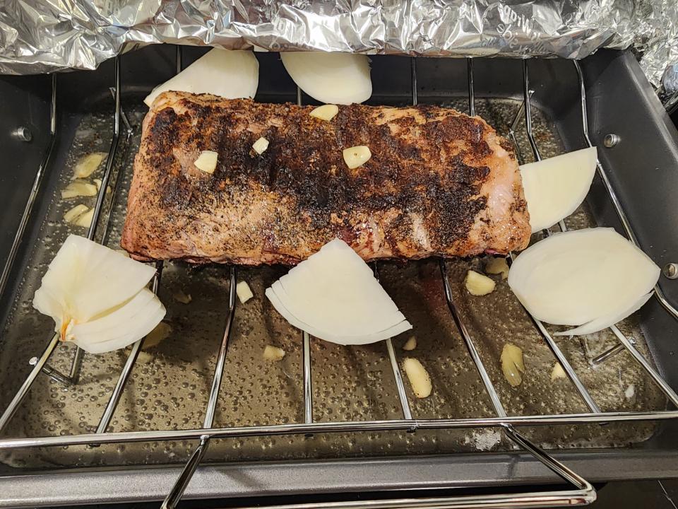 rack of ribs in an oven with onion quarters and chunks of garlic
