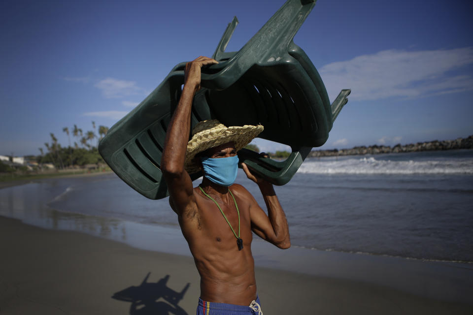 Douglas Yriarte carries rental chairs for tourists on the La Ultima beach which was closed for months amid the COVID-19 pandemic in La Guaira, Venezuela, Friday, Oct. 23, 2020. Strict quarantine restrictions forced the closure of beaches across the country in March and reopened this week in hopes of revitalizing the battered economy. (AP Photo/Matias Delacroix)