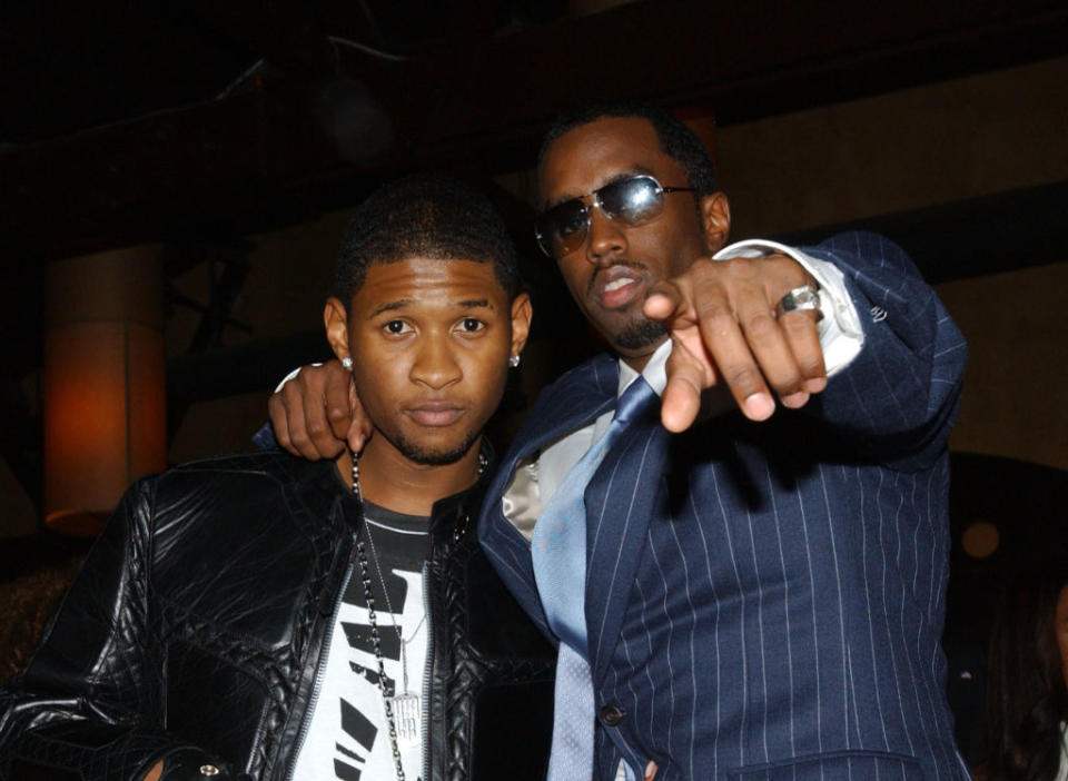 Usher and Diddy posing for the camera, one in a leather jacket and the other wearing a suit