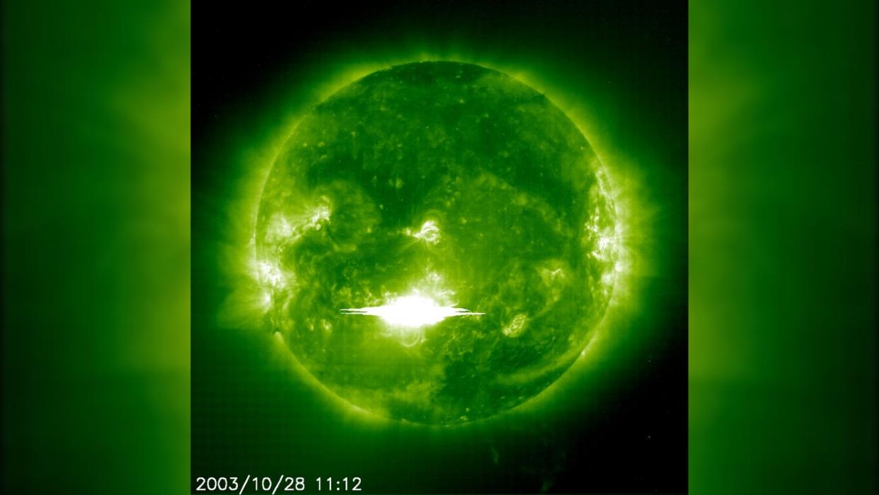  The sun viewed through a green filter with a massive flash of light erupting from its surface. 