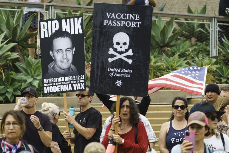 Personas protestan contra los pasaportes de vacunaci&#xf3;n durante una movilizaci&#xf3;n en el parque Tongva en Santa M&#xf3;nica, California, el s&#xe1;bado 21 de agosto de 2021. El cartel de la izquierda dice que esa persona, hermano de quien lo sostiene, falleci&#xf3; despu&#xe9;s de vacunarse. El del centro dice &quot;pasaporte de vacunaci&#xf3;n... Estados Unidos de Am&#xe9;rica&quot;. 