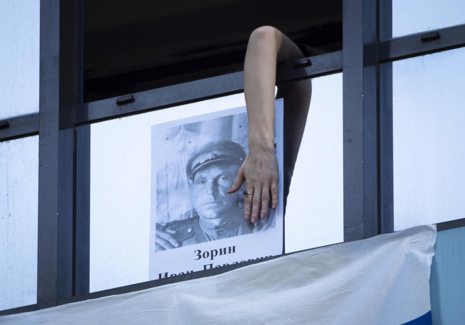 A woman hangs a portrait of her ancestor, a participant in World War II on the window of her apartment during Victory Day celebration in St. Petersburg, Russia, Saturday, May 9, 2020. Victory Day, the anniversary of the defeat of Nazi Germany in World War II, is Russia's most important secular holiday and this year's observance had been expected to be especially large because it is the 75th anniversary, but military parades in Russian cities and a mass procession called The Immortal Regiment were postponed as part of measures to stifle the spread of the virus. (AP Photo/Dmitri Lovetsky)
