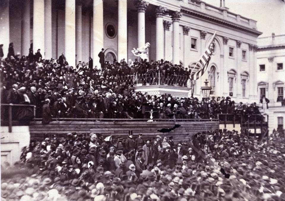 Historical photograph of a large crowd gathered in front of the U.S. Capitol building for Abraham Lincoln's 1861 inauguration. Abraham Lincoln is in the center on a raised platform