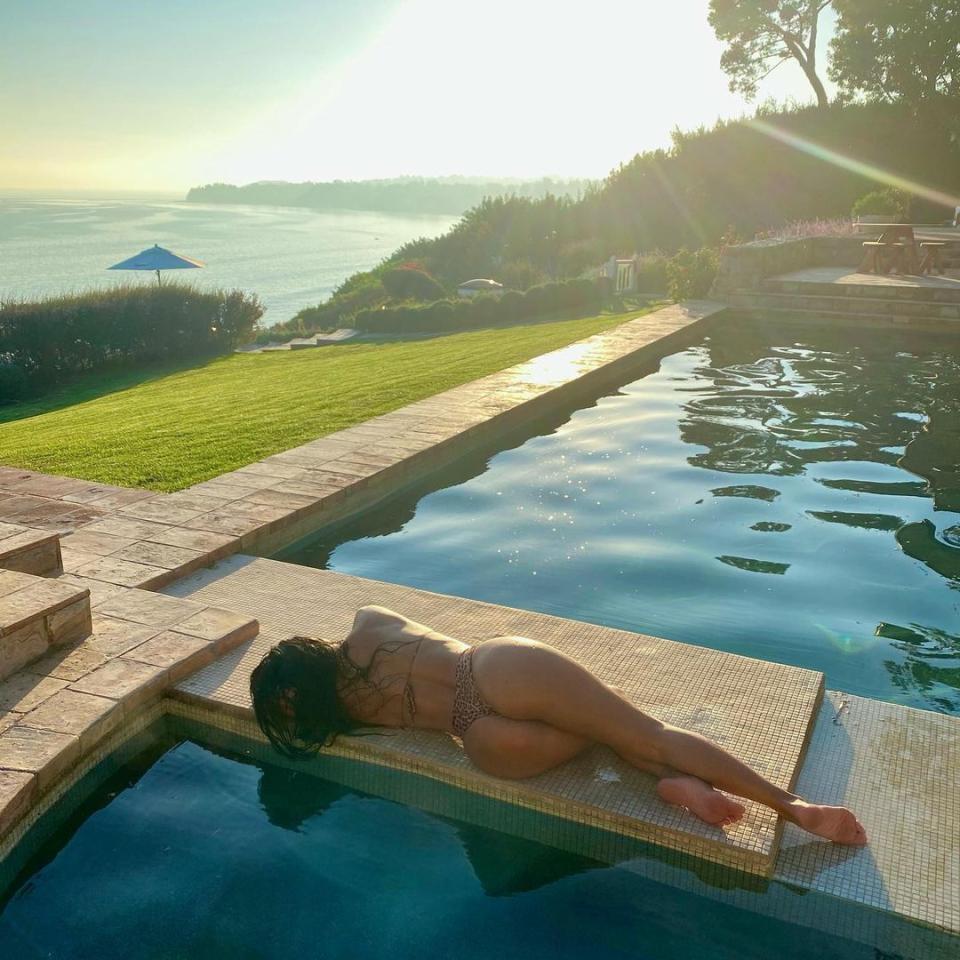 Nicole Scherzinger with her back to the camera lying at the edge of a pool
