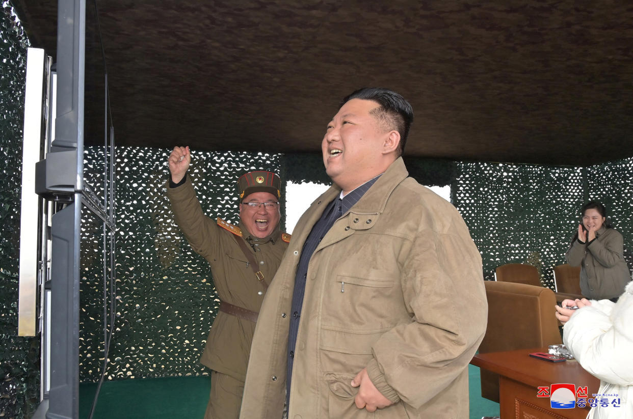 Kim Jong Un, in beige jacket, looks jubilant, as his wife, Ri Sol Ju, applauds in the background, and a North Korean in military uniform pumps his fist in the air. They stand in what appears to be a command center or viewing station lined with metallic soundproofing.