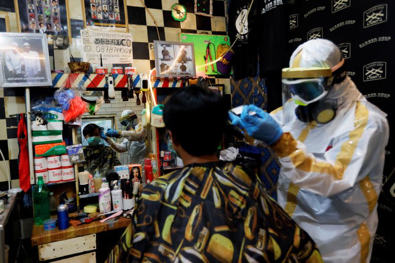 Herman Maulanasyah, a 40-year-old hair stylist, gives a haircut to a customer at his barbershop, while wearing a handmade protective suit in a tribute to the country's medical workers tackling the coronavirus disease (COVID-19) in Bogor