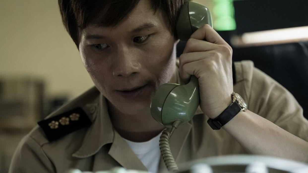 actor hoa xuande holding a cord phone to his left ear with a concerned look on his face in a scene from the sympathizer