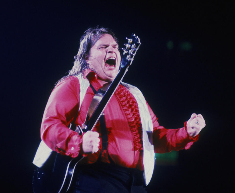 Meat Loaf wearing a red shirt holding a guitar on stage