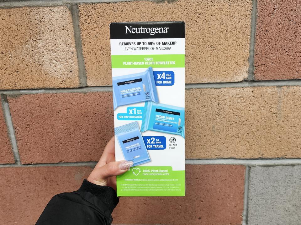 A hand holds a white box with a black Neutrogena label and pictures of blue Neutrogena makeup wipes on it