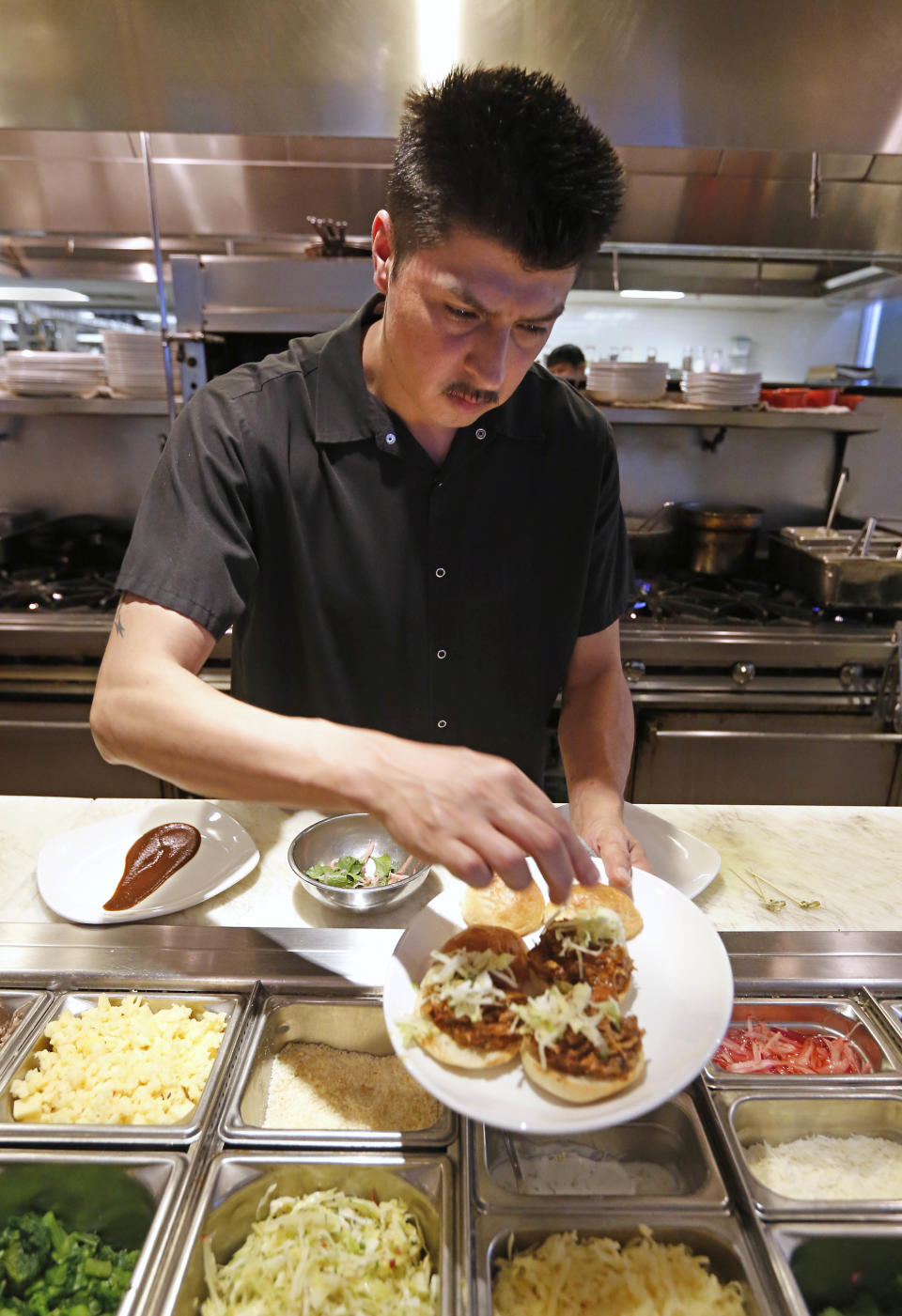 In this photo taken Wednesday, March 12, 2014, line cook Javier Rodriguez uses his bare hands to sprinkle cheese on sliders at the Hock Farm restaurant in Sacramento, Calif. Under a bill signed last year by Gov. Jerry Brown, chefs and bartenders in California must keep bare hands off food going straight to the plate or the drink glass, and must use gloves or kitchen utensils such as tongs. California, where the law took effect Jan. 1 and will begin enforcement starting in July, will join 41 other states banning bare-hand contact with ready-to-eat food. In February,after receiving a petition from bartenders calling for an exemption for the "disposable glove law" the law's author, Assemblyman Richard Pan, D-Sacramento, a pediatrician, has introduced a bill to repeal the new regulation and revisit the entire issue.(AP Photo/Rich Pedroncelli)