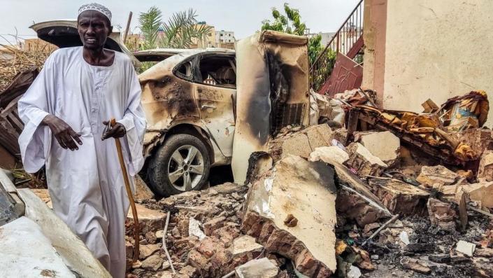 A man inspects the damage as he walks through the rubble of a destroyed car in front of a house which was hit by an artillery shell in Azhari district south of Khartoum on June 6, 2023