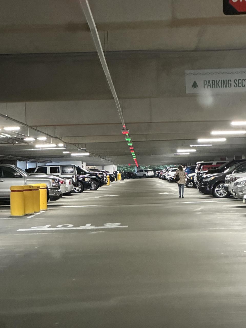 Person walking in a nearly empty, well-lit parking garage with cars parked on both sides. A sign indicates “Parking Section.”