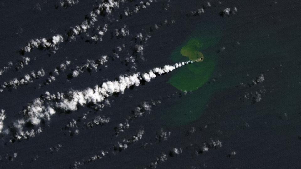 A small green island with a smoking hole forming in the Pacific Ocean