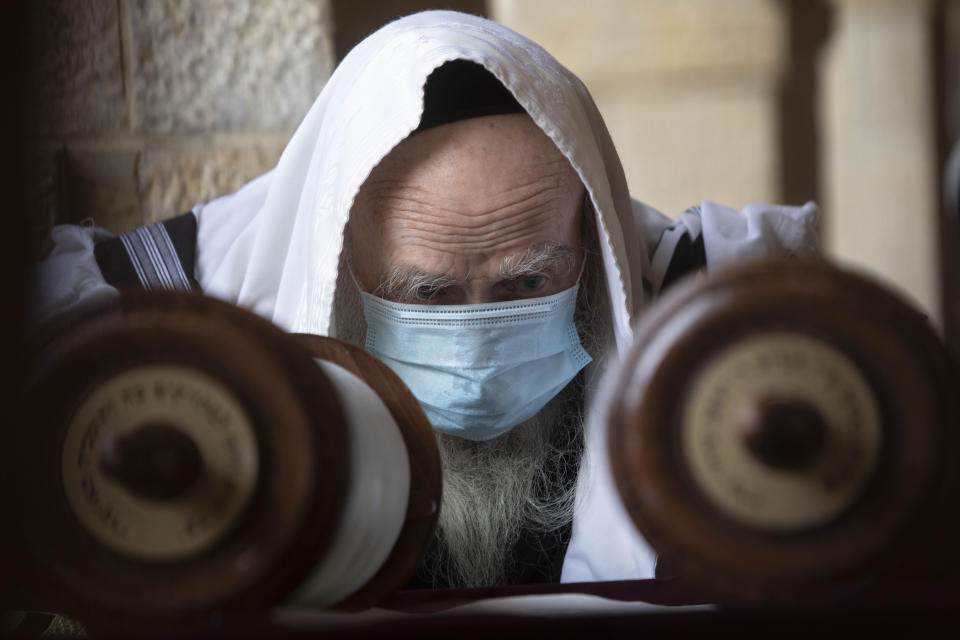 A Jewish man wears a face mask to curb the spread of the coronavirus as he reads from a Torah scroll at the Western Wall, the holiest site where Jews can pray in Jerusalem's old city, Friday, April 10, 2020. (AP Photo/Sebastian Scheiner)