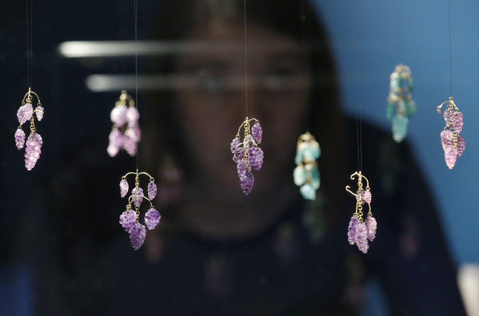 In this Monday, Oct. 7, 2013 photo, a museum employee poses by pendants with bunches of carved amethyst and emerald grape seen on display in an exhibition 'The Cheapside Hoard: London's Lost Jewels' at the Museum of London in the City of London. Diamonds may be forever, but a lot of jewelry doesn’t survive through the centuries. Rings and bracelets get broken up for re-use, pearls decay, gold is melted down. That explains the excitement over a new London exhibition of the Cheapside Hoard _ a trove of almost 500 gemstones and pieces of jewelry from the 16th and 17th centuries, dug up by workmen demolishing a building in London more than 100 years ago. (AP Photo/Sang Tan)