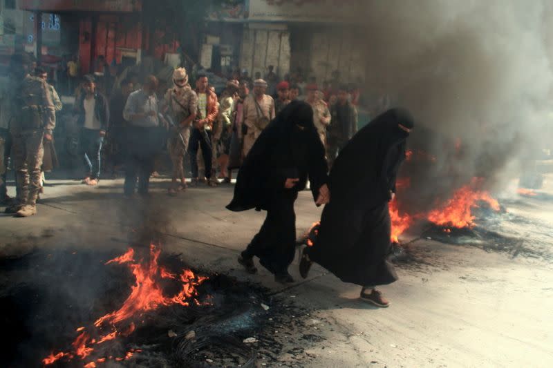 Women run past burning tires during protests against the deteriorating economic situation and the devaluation of the local currency, in Taiz