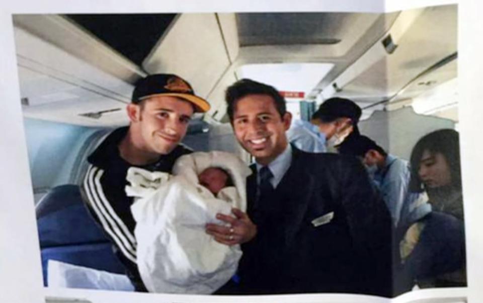 A photograph of birth father Wesley Branch holding Chloe Guan-Branch next to a flight attendant, onboard the Air Canada plane Chloe was born in on May 10, 2015.