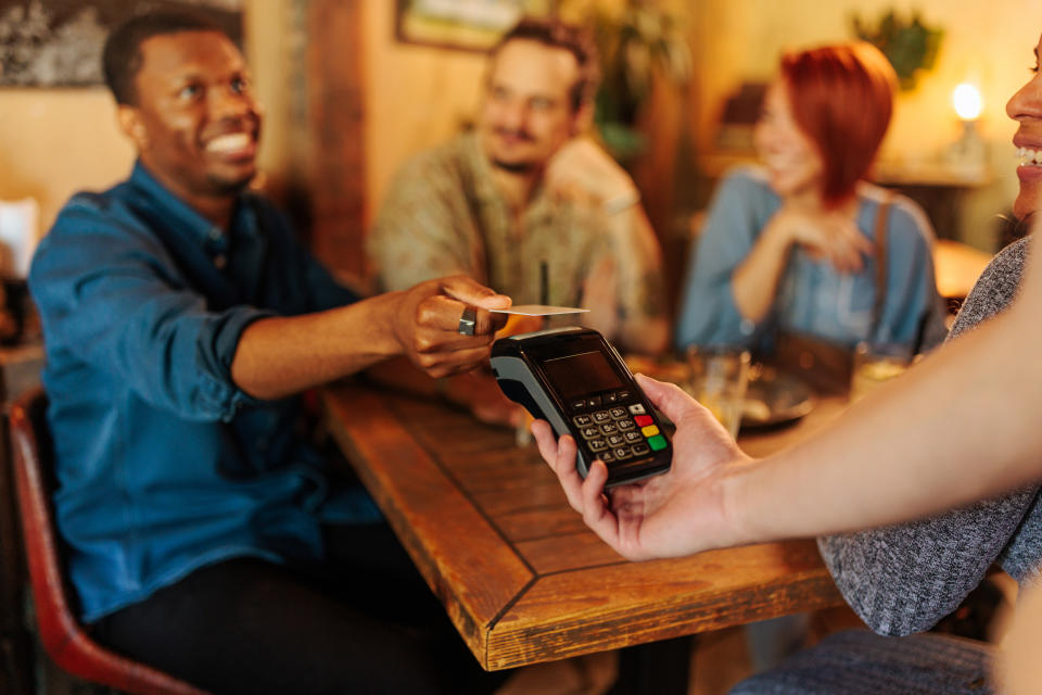 African-American man paying bill in a restaurant by swiping the credit card.