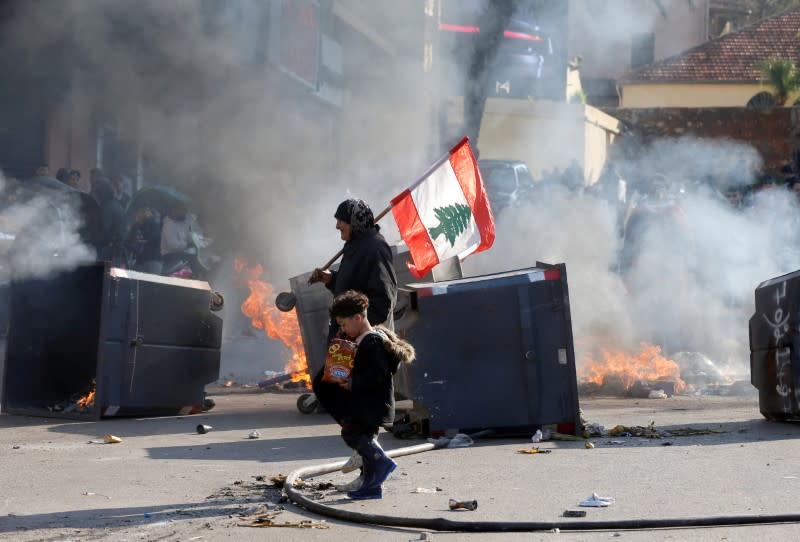 A protestor holding the Lebanese flag walks near burning barricades during a protest over economic hardship and lack of a new government in Beirut