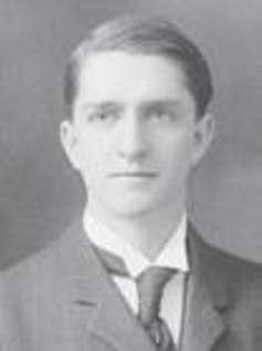 A young man in a dark jacket, white shirt and dark tie.