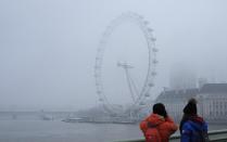The London Eye ferris wheel is photographed by tourists who stand on Westminster Bridge on a foggy day in London, Monday, Jan. 23, 2017. Freezing fog covered the capital on Monday as cold weather conditions continued. (AP Photo/Alastair Grant)