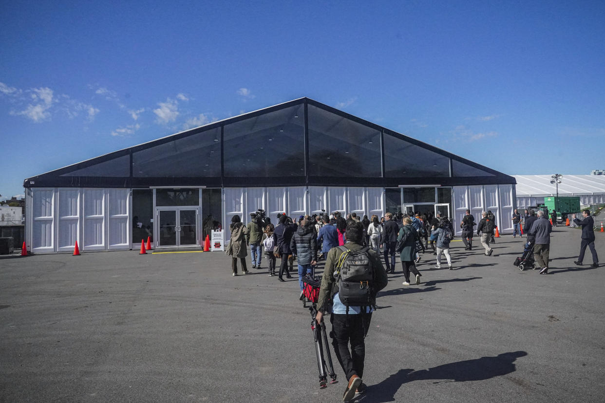 Media arrive for a tour at the Randall's Island Humanitarian Emergency Response and Relief Center, center, a complex of giant tents to serve as a temporary shelter for migrants being bused into the city by southern border states, Oct. 18, 2022, in New York. The shelter will start taking in single adult men on Wednesday, Oct. 19, with facilities including laundry, regular meals and access to international calls. (AP Photo/Bebeto Matthews)