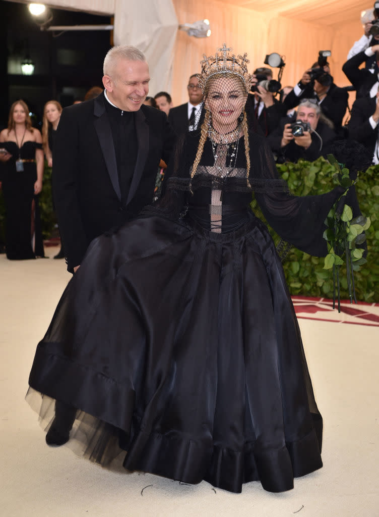 Person in black gown with beaded headpiece and other in suit on a red carpet