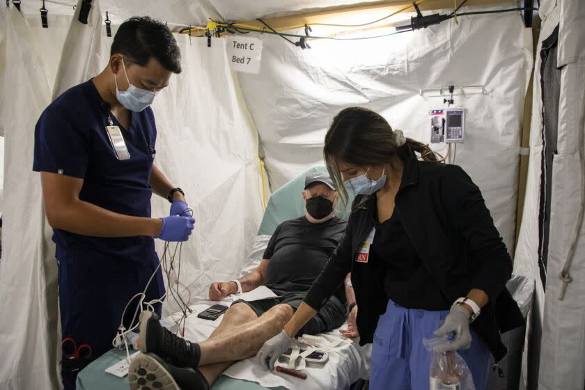 Encinitas, CA - November 11: David Tran, an emergency department technician, left, prepares to put a cardiac monitor on Mark Swenson, 71, of Oceanside, center, as he has his blood drawn by Jessica Smith, a registered nurse, after having low sodium at Scripps Memorial Hospital Encinitas on Friday, Nov. 11, 2022 in Encinitas, CA. Scripps recently opened an overflow tent outside of the hospital after an increase of flu patients. (Ana Ramirez / The San Diego Union-Tribune)