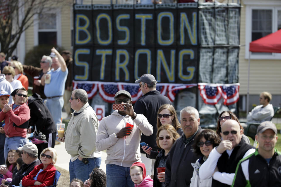 Race fans alongside a "Boston Strong" slogan, watch the 118th Boston Marathon Monday, April 21, 2014 along the race course to Boston. (AP Photo/Steven Senne)