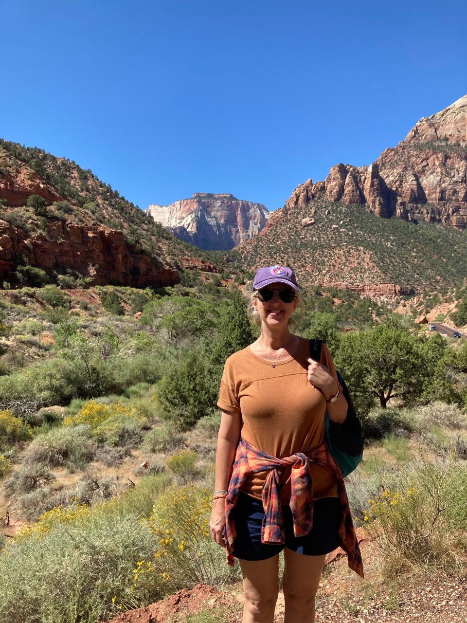 Women wearing orange shirt, purple baseball cap, and black shorts in Zion National Park, Courtenay Rudzinski airbnb review