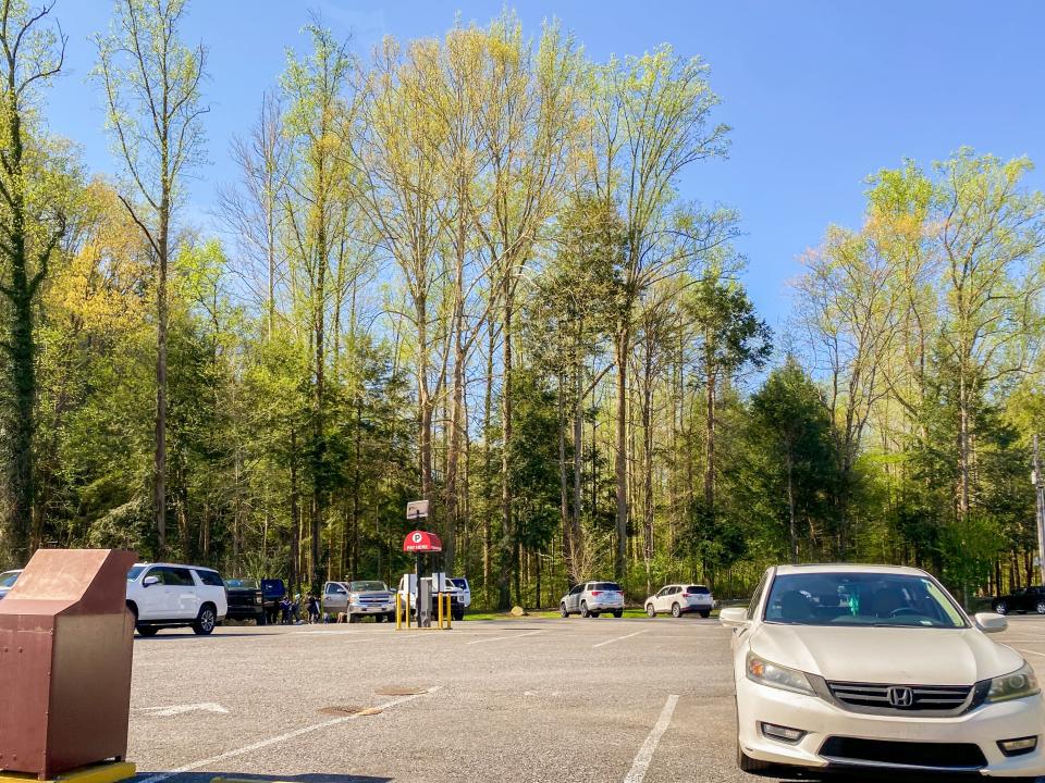 A parking lot is mostly empty with green trees in the background. The sky behind is clear and blue