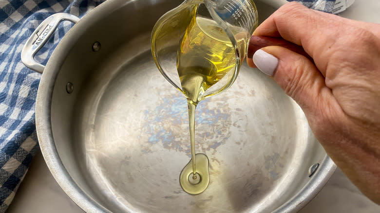 hand adding oil to pan